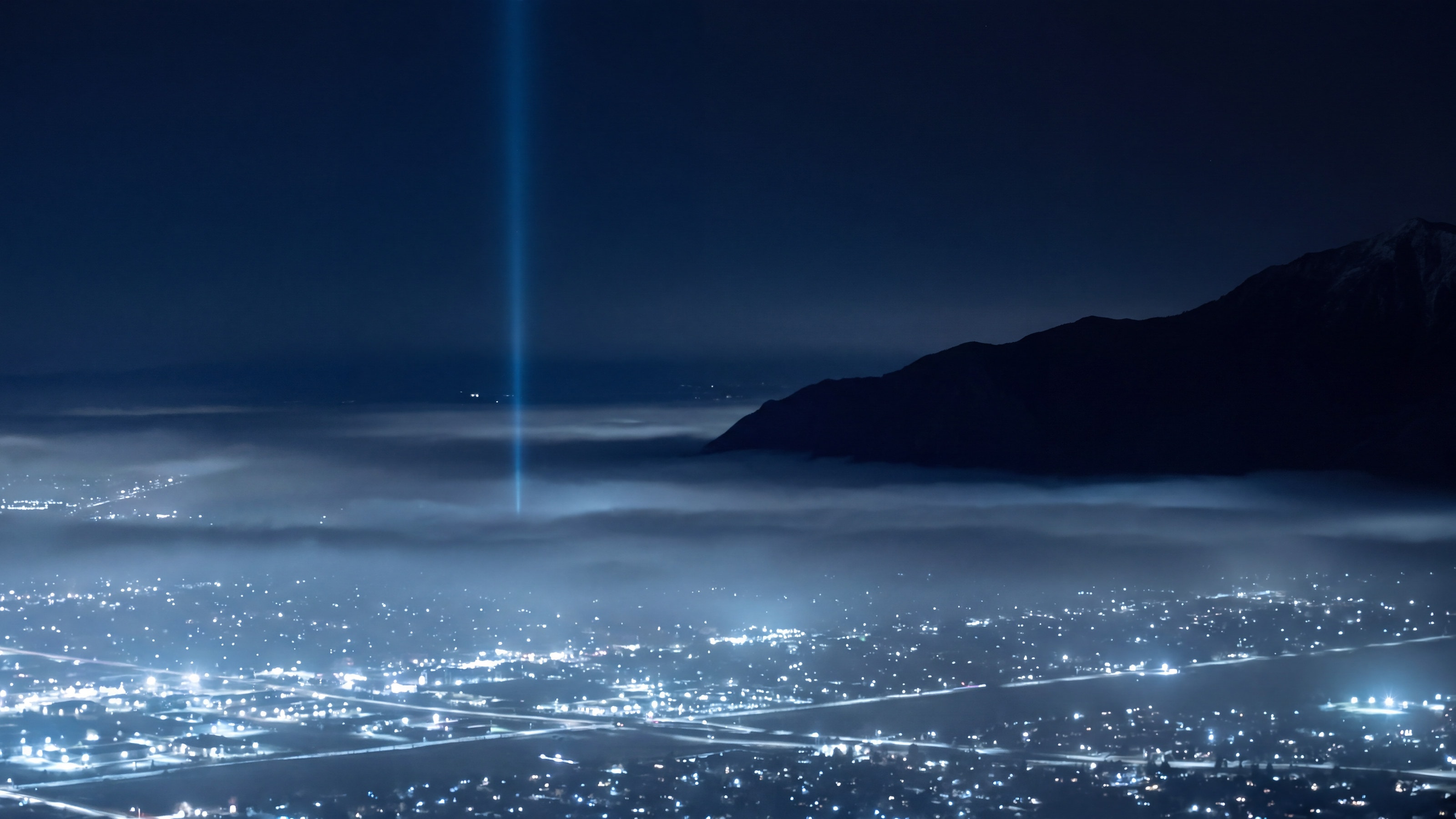 Utah Valley at night under low fog, with a single beam of light rising from the valley